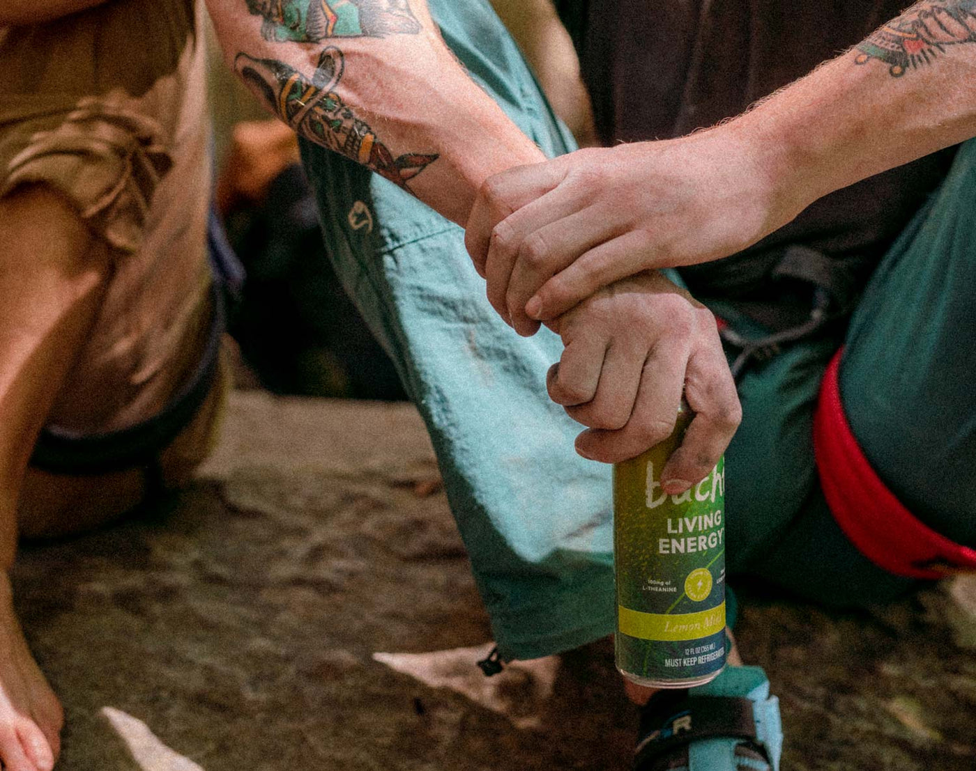 Tattooed person holds a can of Living Energy while rock climbing