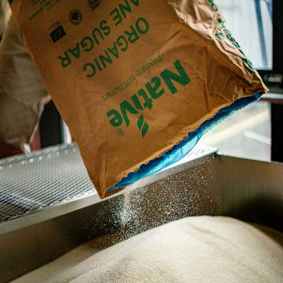 A tilted big brown bag of cane sugar with sugar pouring out of it onto a metal shelf.